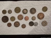 Photo showing 18 assorted coins from different countries with varying sizes and designs laid on a white cloth.
