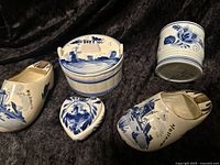 Overview of all five Delft Blue pieces including two ceramic shoes, a heart-shaped trinket box, a covered trinket dish, and a small cup.