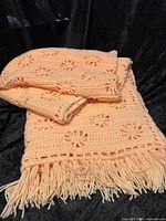 Full view of afghan blanket folded, showing peach pink color, floral crochet pattern and fringe