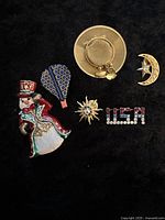 Six vintage jewelry pins on black background with quarter for size comparison