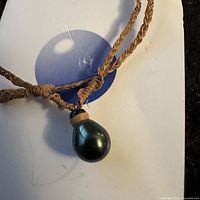 Close-up of the single large black Tahitian pearl pendant on brown braided cord showing the pearl shape and texture.