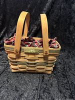 Front view of woven wooden basket with two upright wooden handles and plaid fabric liner visible inside.