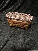 Front angled view of woven oval basket with red and natural colors, cloth liner with red and white stripes folded over top edge.