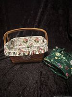 Photo of the Longaberger Mother's Day 1997 basket with floral cloth liner inside and green floral cloth liner placed beside it against black background.
