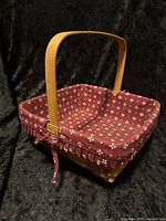 Square basket in natural wood with arched handle and red floral cloth liner with ruffled edges and bow.