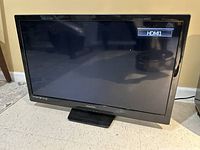 Full front view of Magnavox 32 inch television on floor, screen off showing reflection.