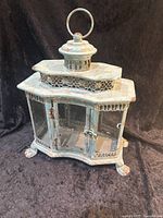 Front view of the metal candle lantern showing the overall shape, glass door, claw feet, and vented top with ring handle.