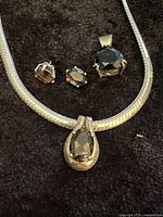 Close up image showing sterling silver snake chain necklace with dark amber teardrop pendant and matching amber stone stud earrings.