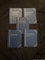 Five US coin collection books displayed on dark fabric, showing covers with embossed gold text for Liberty Standing Half Dollar (two books), Jefferson Nickel, Lincoln Head Cent, Buffalo Nickel.