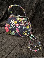 Front and partial side view of navy Vera Bradley quilted cloth crossbody bag with multicolor floral design, showing metal clasp and handle.
