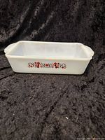Full view of the rectangular opaque white glass baking dish with floral pattern on the side and two small handles.