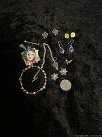 Wide shot of all jewelry items including clown brooch, bracelets, earrings, and pins along with a quarter for size reference.