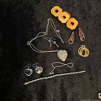 Full assortment of vintage jewelry on black surface including necklaces, earrings, bracelet, and orange clip-on earrings
