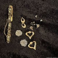 Vintage jewelry lot on black fabric including a multi-link bracelet with floral and bird inlay, various earrings, heart and flower pendants, with a quarter for scale.