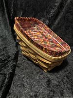 Side angle view of the Longaberger sleigh basket showing natural wood weave and fall floral cloth liner with clear plastic liner inside.