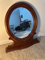 Full view of the vintage standing oval mirror showing its curved wooden frame and base standing on carpet.