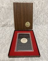Wooden display box open showing the proof dollar in plastic case seated in red velvet interior with gold seal on lid.