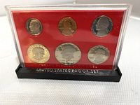 Clear plastic case containing 6 US proof coins (dollar, half dollar, quarter, dime, nickel, penny) with red backing and black plastic stand labeled 'UNITED STATES PROOF SET'.