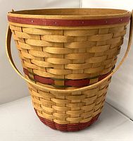 Front side view showing basket shape, natural wood color with red and green woven accents, and handle.