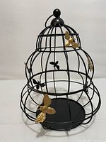 Front angle of black metal beehive shaped basket decorated with gold and black bees, showing hanging loop on top and base plate.
