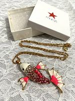 Goldtone fish pendant necklace with pink rhinestones and enamel on white lace background, accompanied by Macy's jewelry box.