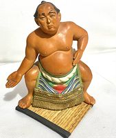 Front view of ceramic sumo wrestler figure standing on woven mat base, showing detailed paint and figure posture.