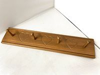 Full front view of wooden peg rack showing four pegs and three engraved hearts along the length.