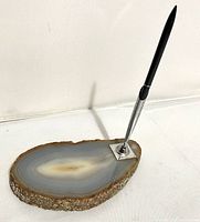 Photo shows sliced agate base with concentric bands and polished top surface with metal pen holder and black pen inserted.
