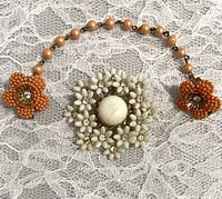 Top view of the white flower brooch pin in center with orange beaded flower sweater clips connected by orange bead chain on side