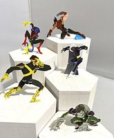 Photo showing five miniature plastic X-Men Evolution figures posed on white hexagonal stands. Characters include a running male figure in black/yellow, crouching figure in green, figure with claws in brown, blue/black figure with raised hand, and a black/white figure with long hair.