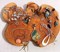 Five signed necklaces arranged on wood display showing varying styles including silver coin chain, beaded and pendant necklace.