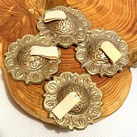 Four vintage finger cymbals with elastic straps arranged on a wooden slab. Metallic with floral scalloped edges and embossed designs.