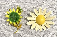 Two vintage flower pins on lace background, showing front views and visible wear.