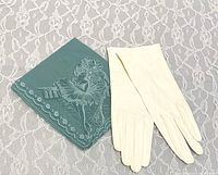Pair of small white gloves next to a turquoise handkerchief with ballerina and Harlequin design on lace background