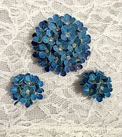 Full set laid out on lace background showing brooch and two clip earrings with blue flower enamel design and rhinestone centers