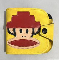 Front exterior of wallet showing yellow synthetic leather with large Julius the Monkey applique wearing the red Devo Energy Dome hat and snap button closure.