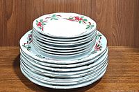 Stack of 8 dinner and 8 dessert plates with Christmas poinsettia design, showing the full set from a side angle.