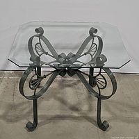 Glass top side table showing metal butterfly base from front angle.
