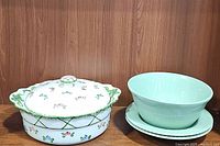 Floral lidded dish, large green bowl and plate, and pair of smaller green pasta bowls on a wooden surface.