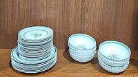 Stack of dinner plates, dessert plates and bowls showing green thistle pattern and scalloped edging.