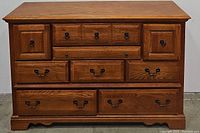 Front view of 9-drawer oak dresser showing all drawers closed, highlighting wood grain and metal handles.