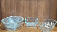 Four nested round Pyrex glass bowls, one square Pyrex glass dish, and one divided oval Pyrex glass dish shown on wooden background.