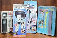 Lot items displayed on wooden surface: indoor alarm, Drain Buster tool, Twin Draft Guard insulation, Water Ninja scraper