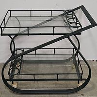 Full view of the two-tier black iron bar cart with glass shelves and circular bottle holders on both levels.
