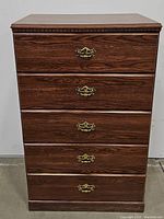Front view of the chest of drawers with all five drawers closed, showing wood grain finish and brass handles.