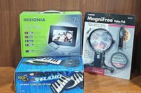 Three boxed items: Insignia digital picture frame, Carson MagniFree magnifier kit, and Rock It! Studio flexible roll-up piano.
