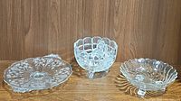 Photo showing all three dishes together: etched glass handled dish, frosted three-footed crystal dish, and swirl scalloped pressed glass dish.