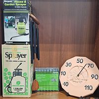 Photo shows boxes for two garden sprayers, Burgess and Greenlawn, and an outdoor thermometer with leaf design.