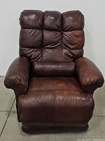 Front view of the brown leather recliner chair showing padded armrests, cushioned backrest with button detailing, and seat cushion with visible wear.