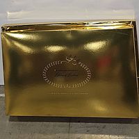 Closed gold presentation box with decorative writing and design on the front, which appears to be packaging for the dress.